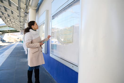 Full length side view of a female traveler standing at a board with train schedule information