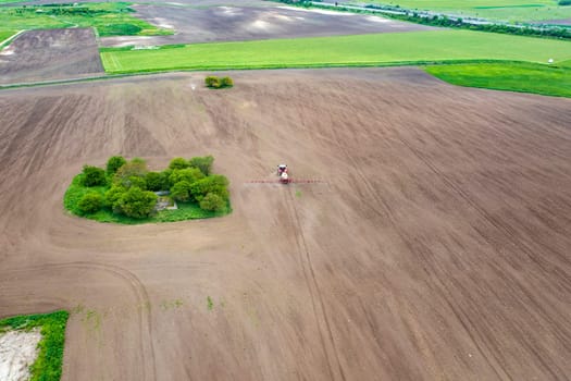 Aerial view of tractor spraying aerosol on a grain fields