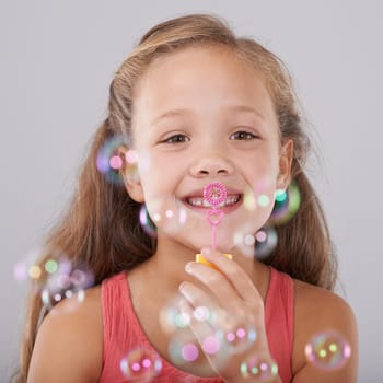 Portrait, kid and blowing bubbles in studio by toy, happiness and fun games for hand eye coordination. Little girl, face and learning to play on soap wand, development and sweet by gray background