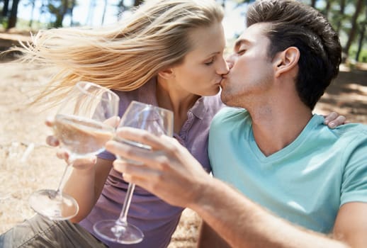 Couple, kiss and wine in nature or forest for celebration of love, holiday and valentines day. Man and woman together with glasses, alcohol drinks and toast on outdoor date for anniversary in woods