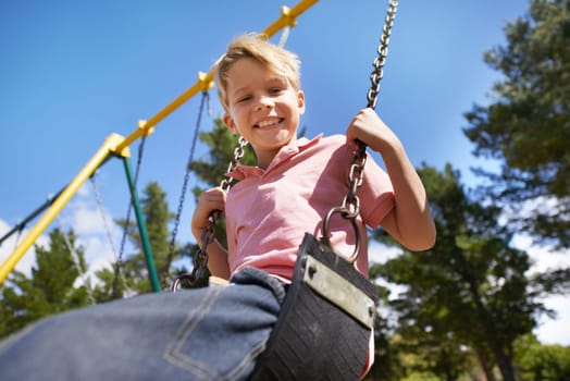 Child, swing and fun on playground in portrait, smile and outdoor adventure in childhood for recreation at park. Happy male person, active and energy on equipment, boy and play on vacation or holiday