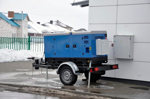 Blue backup generator on trailer. Mobile backup generator near the building in winter in cold weather.