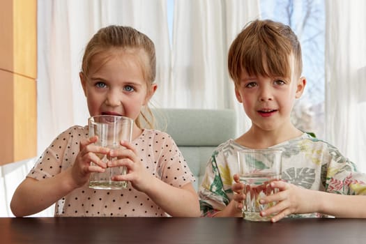 Brother and sister sit at table drinking water from glasses