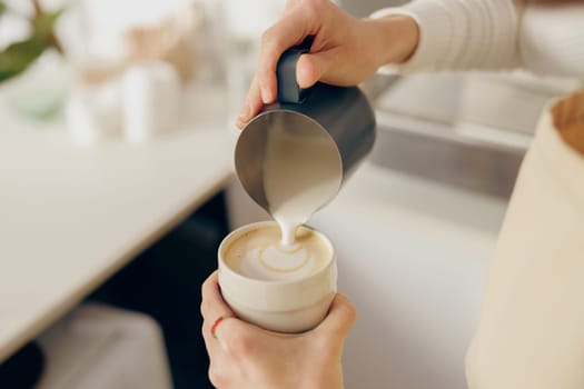 Close up of female barista makes coffee and pours it into a mug while working in coffee shop