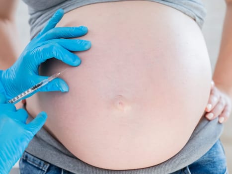 Doctor gives an injection in the stomach of a pregnant woman.