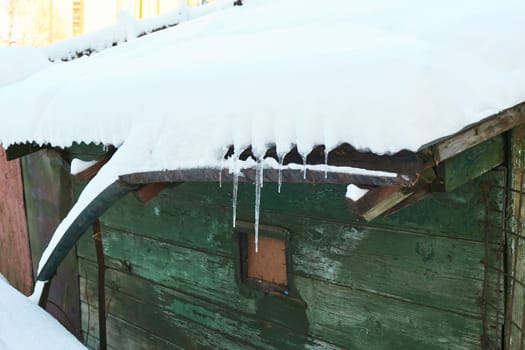 old green wooden house under the snow. Icicles