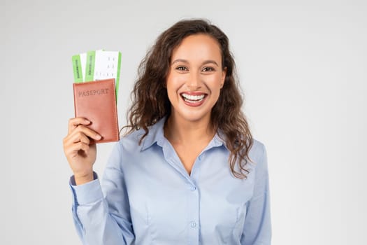 A cheerful woman with curly hair, wearing a blue shirt, happily displays her passport
