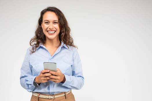 An engaging young woman with curly hair and a bright smile looks up from her smartphone
