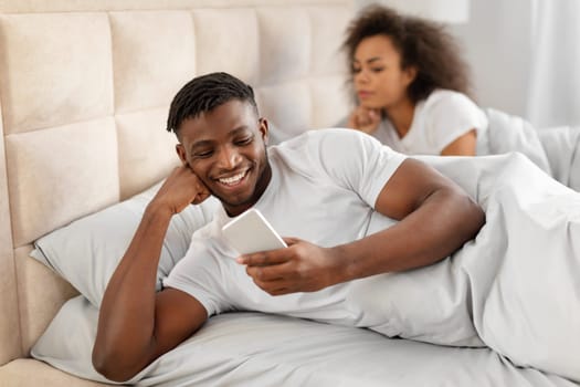 Concerned Black Wife Looking At Husband Texting On Phone Indoor