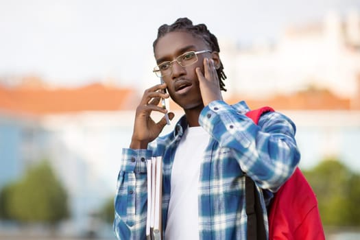 Distressed African American student guy talks on cellphone outdoors