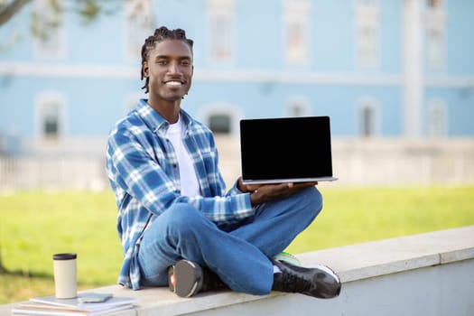 Happy black guy showcases blank screen on his laptop outside