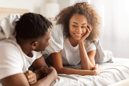 Playful african american spouses flirting in bed under blanket indoors
