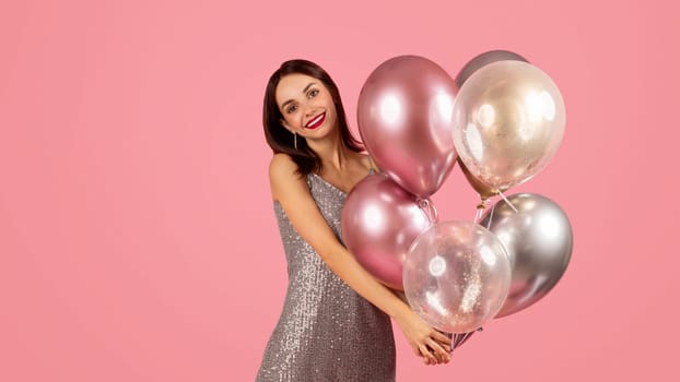 Smiling woman in a glamorous sequin dress holding a cluster of metallic and transparent balloons
