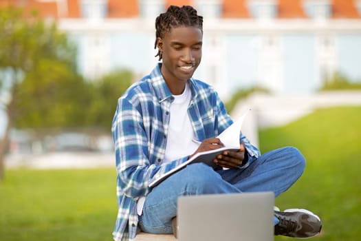 black student man studying with laptop and workbooks at park