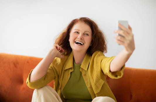 Radiant senior woman laughing joyfully while taking selfie on smartphone at home