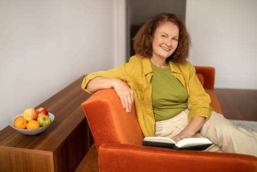 Happy senior woman reading book while relaxing on couch at home