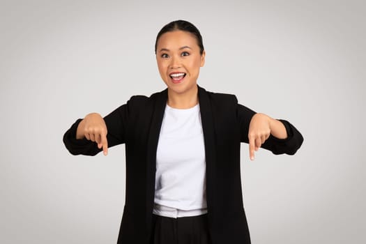 Enthusiastic Asian businesswoman with a broad smile pointing downwards with both hands
