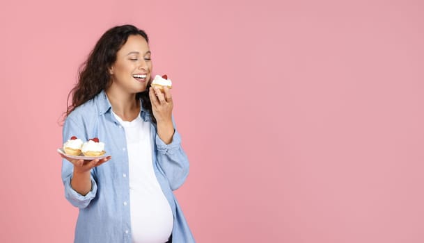 Hungry Expectant Lady Eating Sweets Standing Over Pink Studio Background