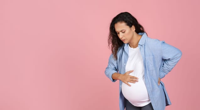 Young pregnant woman suffering from labor pains on pink