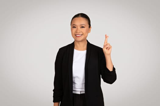 A poised Asian businesswoman in a smart black jacket displays a victory sign with a joyful