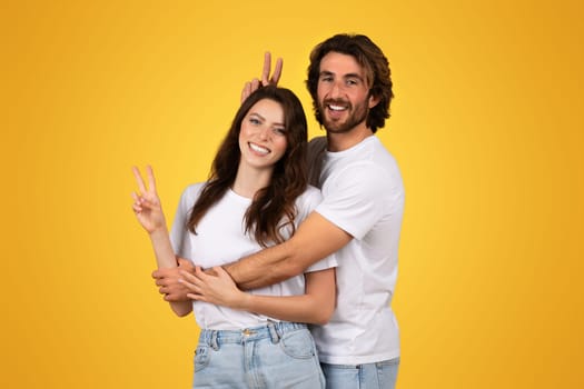 Happy couple in white shirts posing with the woman showing a peace sign and the man playfully