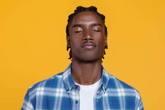 Peaceful young black man with closed eyes standing against yellow background