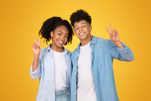 Happy young African American woman and man making peace signs with their hands