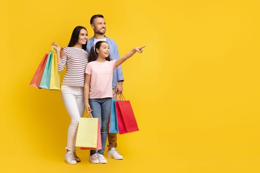 Excited family with shopping bags in hand pointing aside at copy space