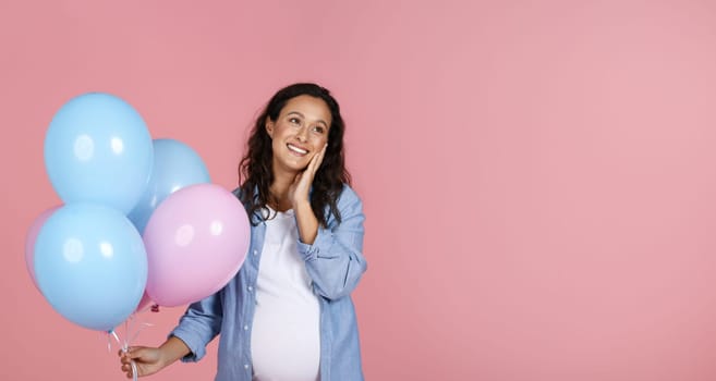 Cute young pregnant woman with pink and blue balloons