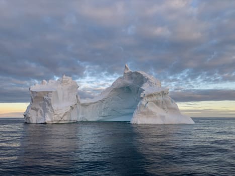 A huge high breakaway glacier drifts in the southern ocean off the coast of Antarctica at sunset, the Antarctic Peninsula, the Southern Arctic Circle, azure water, cloudy weather