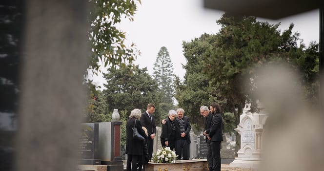 People at a funeral, death and graveyard with family mourning outdoor, grief and loss with coffin. Cemetery, ceremony and sad, goodbye and burial service with support, comfort and empathy at memorial