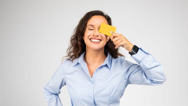 Smiling young woman playfully covering one eye with a yellow credit card