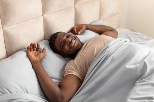 Well rested black man wakes up stretching arms in bed