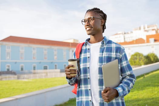 Successful African American young man holds laptop and coffee outside