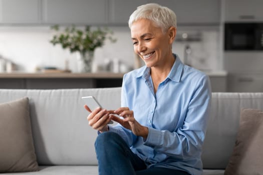 Happy Mature Woman Using Smartphone Gadget And Applications At Home