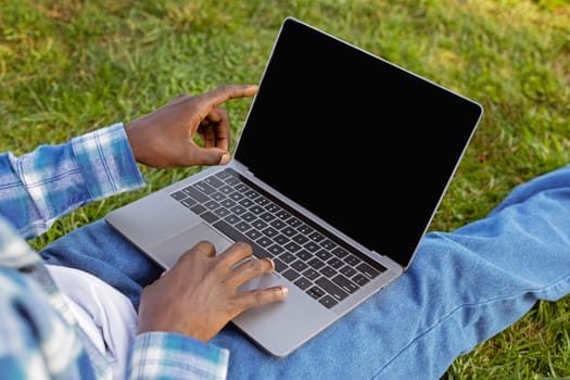 Cropped of black guy using laptop with empty screen outdoor