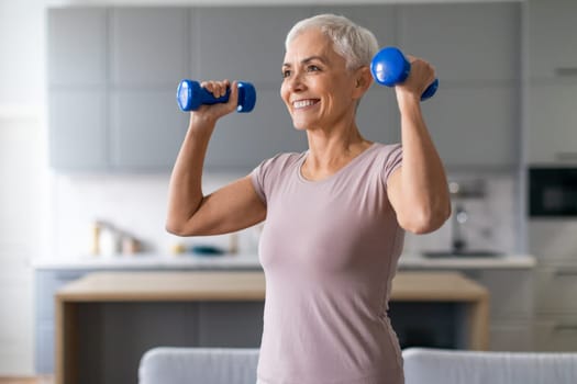 Active European senior lady stays fit exercising with dumbbells indoor