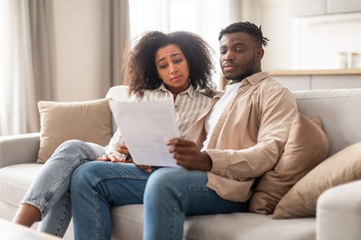 Stressed married young black couple looking at loan documents indoor