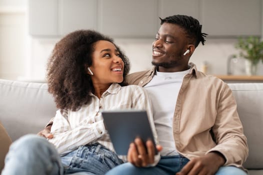 Relaxed african american couple wearing earbuds listening music together indoors