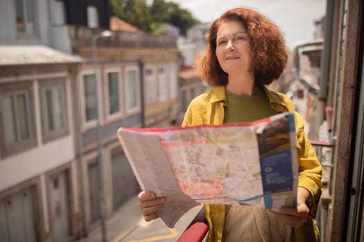 Curious senior woman exploring city map while standing on sunny balcony
