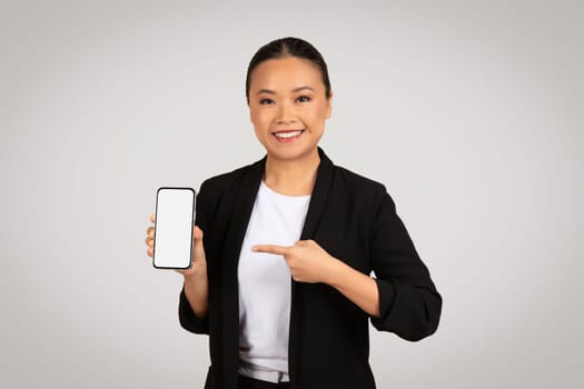 Smiling Asian businesswoman presenting a smartphone with a blank screen