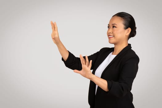 Confident Asian businesswoman with a pleasant smile reaching out to interact with a virtual interface