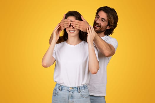 Smiling man surprises a woman by covering her eyes from behind with his hands