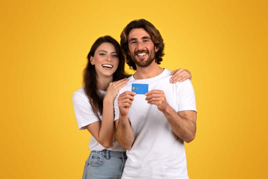 Radiant couple smiling and holding a blue credit card together