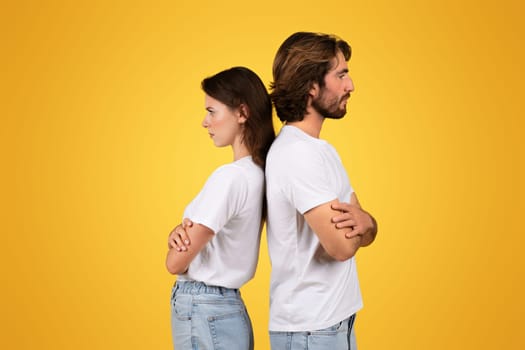 A couple in white t-shirts and blue jeans stands back to back with crossed arms