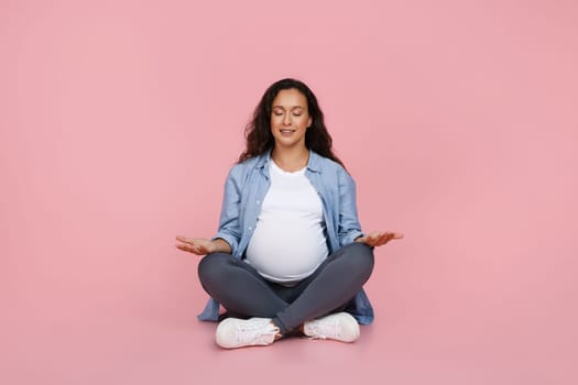 Portrait of positive pregnant woman meditating on floor