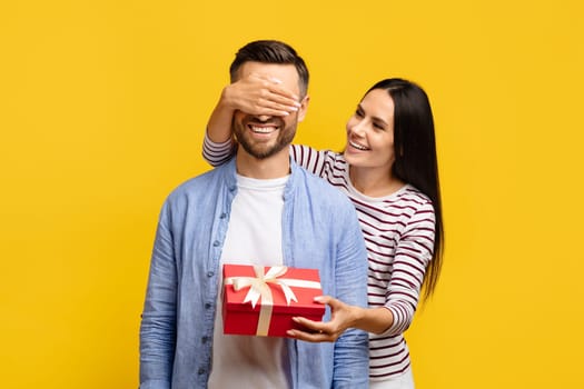 Surprise Gift. Romantic woman covering boyfriend's eyes and giving present