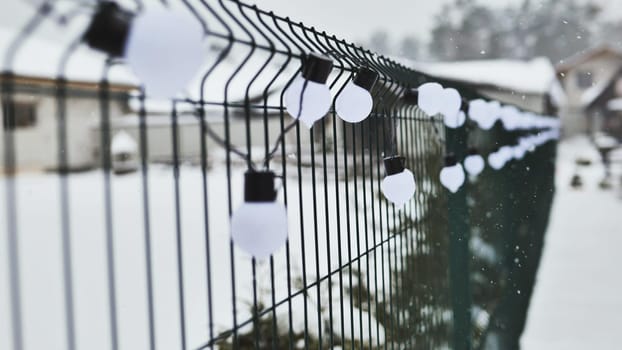 A white garland of bulbs on a fence in winter.
