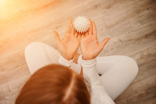 Athletic slim caucasian woman doing thigh self-massage with a massage ball indoors. Self-isolating massage