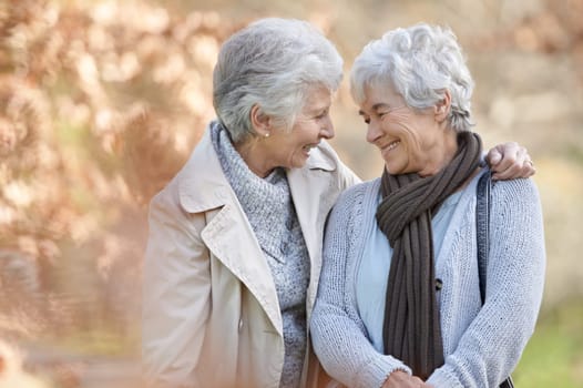 Senior women, happy and support in park by autumn leaves, together and bonding on retirement in outdoor. Elderly friends, hugging or communication on vacation in england, smile or social in nature.